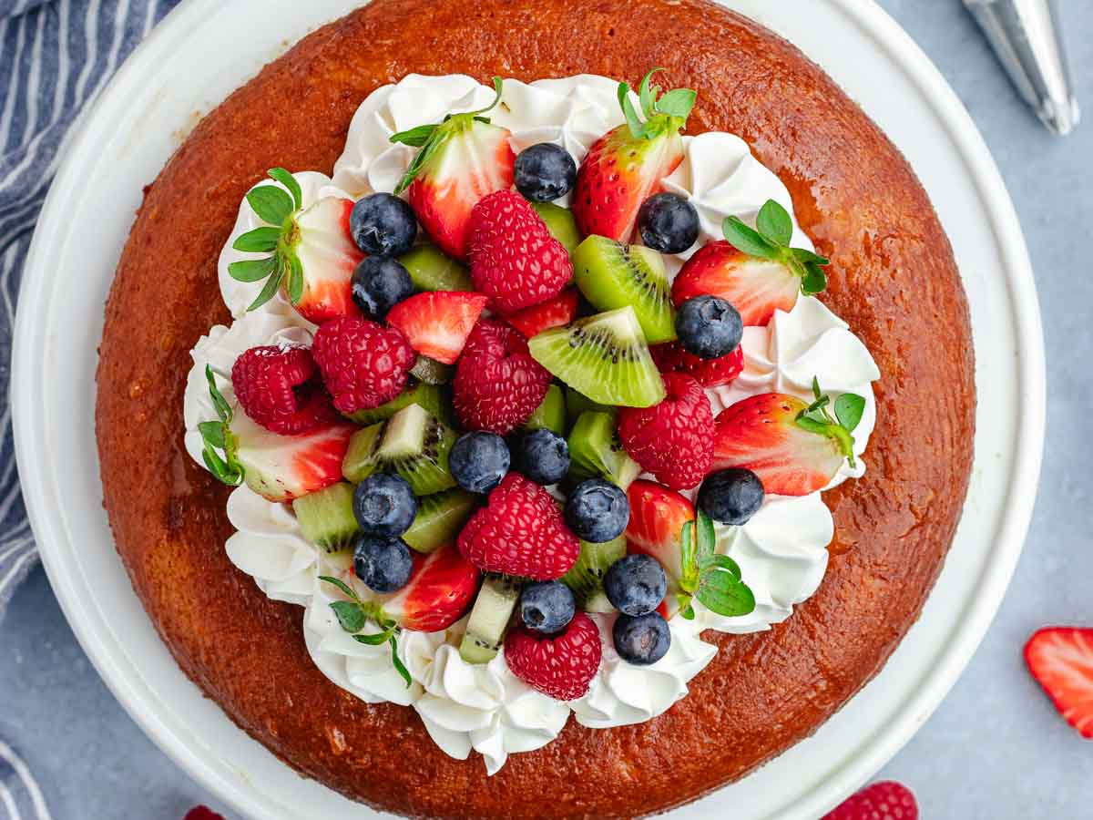 Overhead view of a cake topped with fruit and whipped cream.