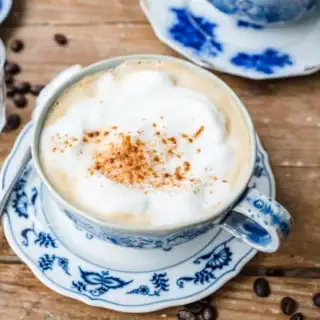 Zoomed out view of top view of a coffee mixture, topped with foam on top of a blue and white saucer.