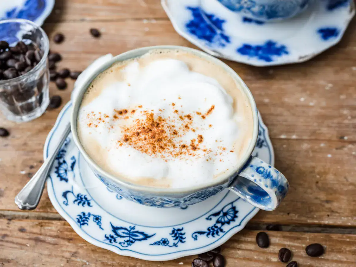 Zoomed out view of top view of a coffee mixture, topped with foam on top of a blue and white saucer.