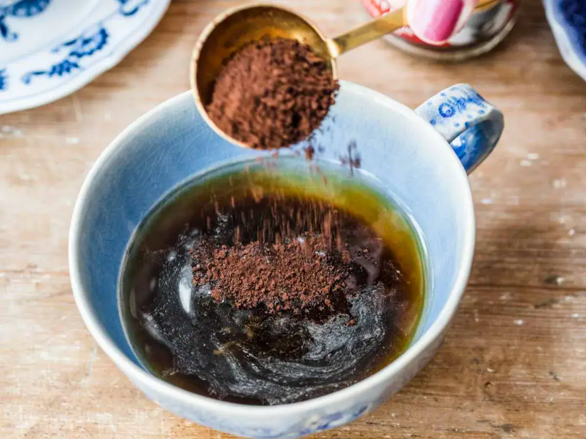 Instant espresso being added to hot water in a light blue mug.