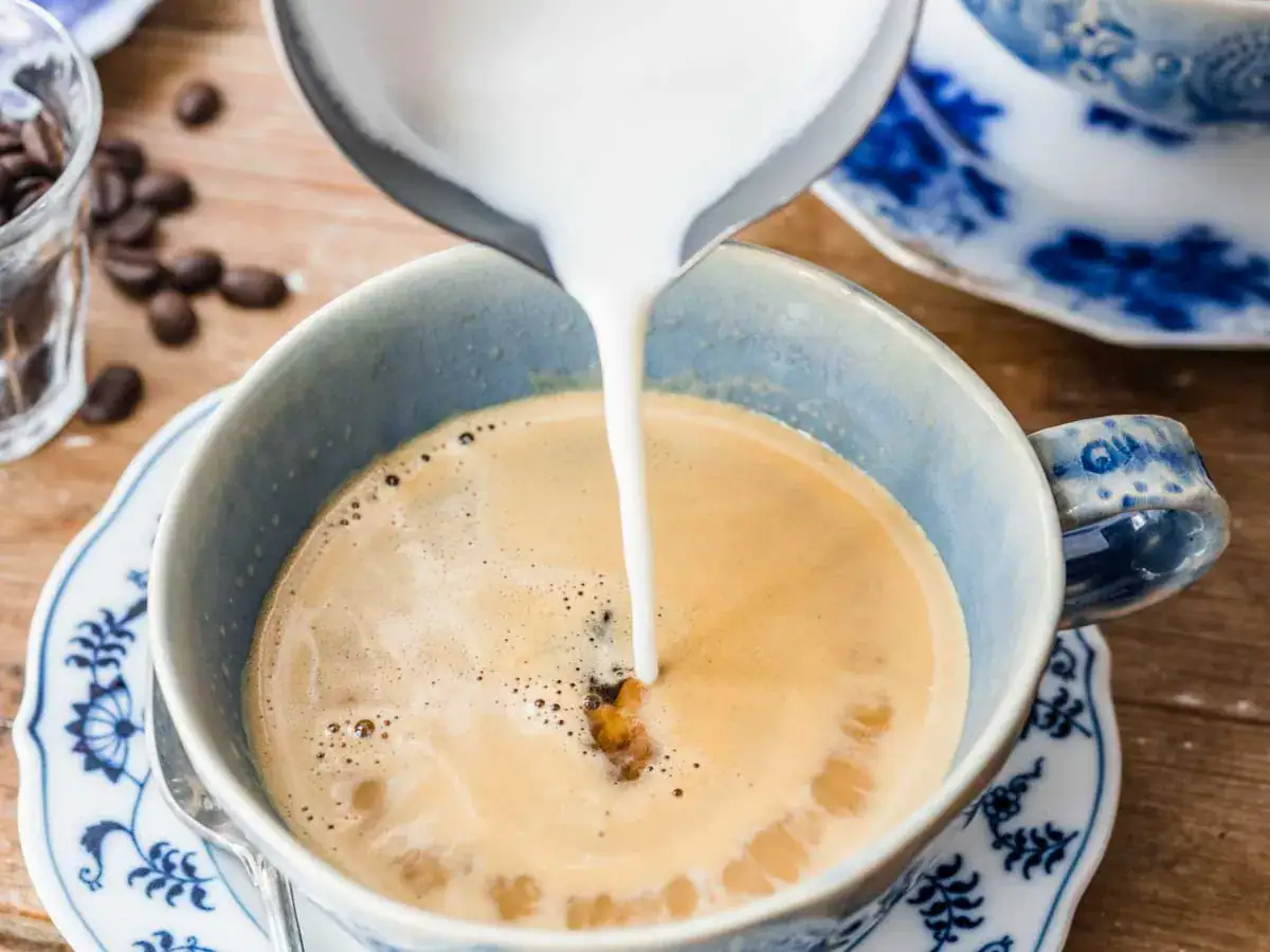 White liquid being poured into a light blue mug filled with coffee.