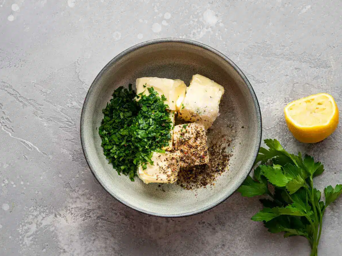 Stone colored bowl filled with butter, a green herb and other seasonings
