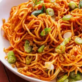 Garnished spicy stir fry noodles in a shallow bowl