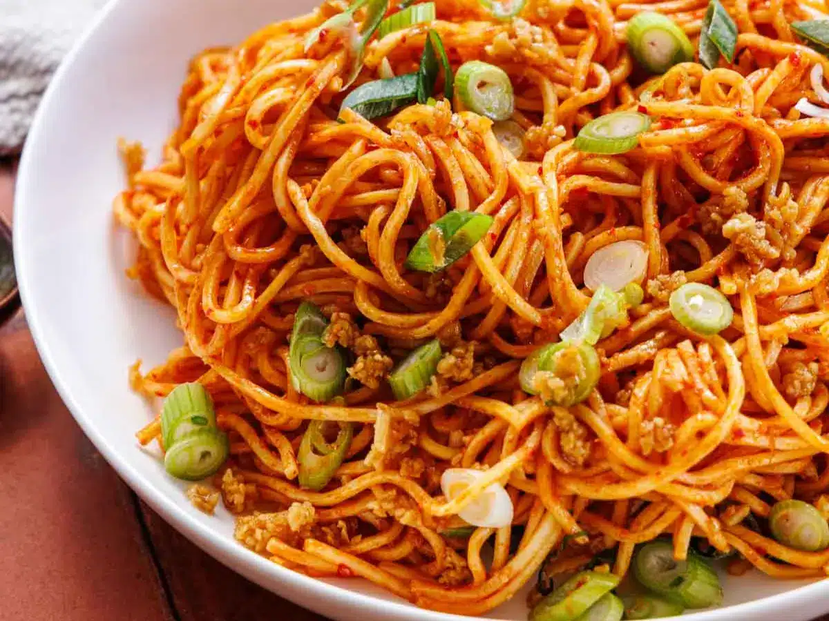Garnished spicy stir fry noodles in a shallow bowl
