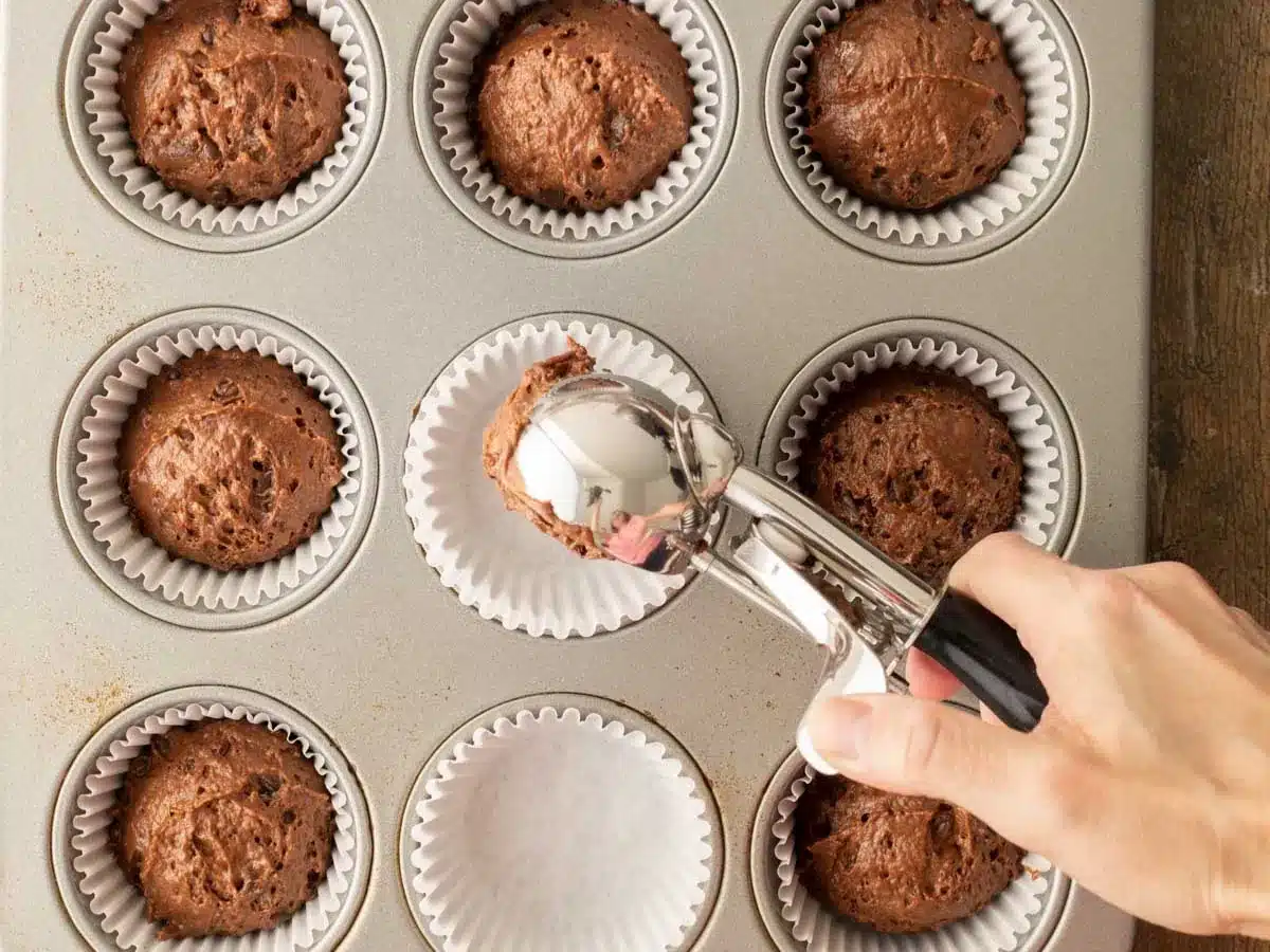 Raw dough in scoop being placed into muffin tin.