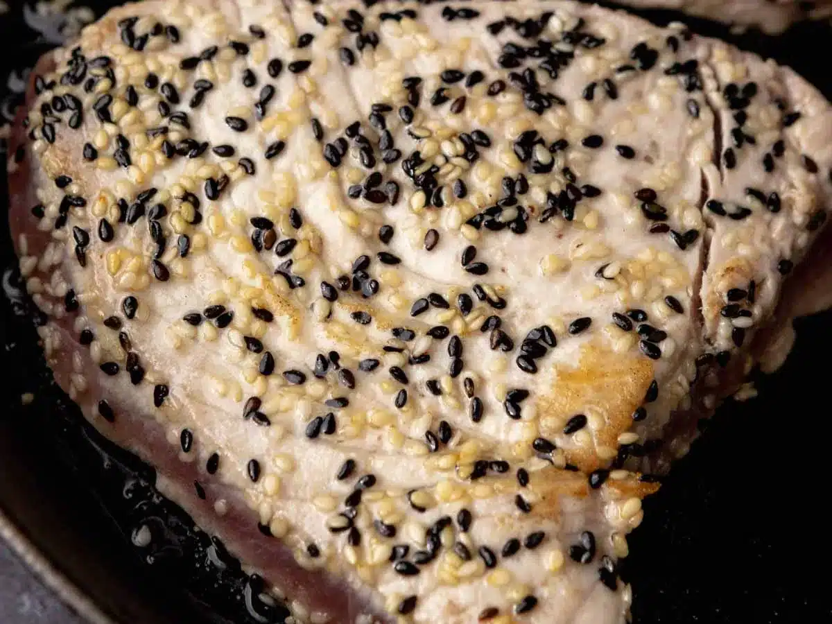 Medium rare ahi in pan topped with sesame seeds.