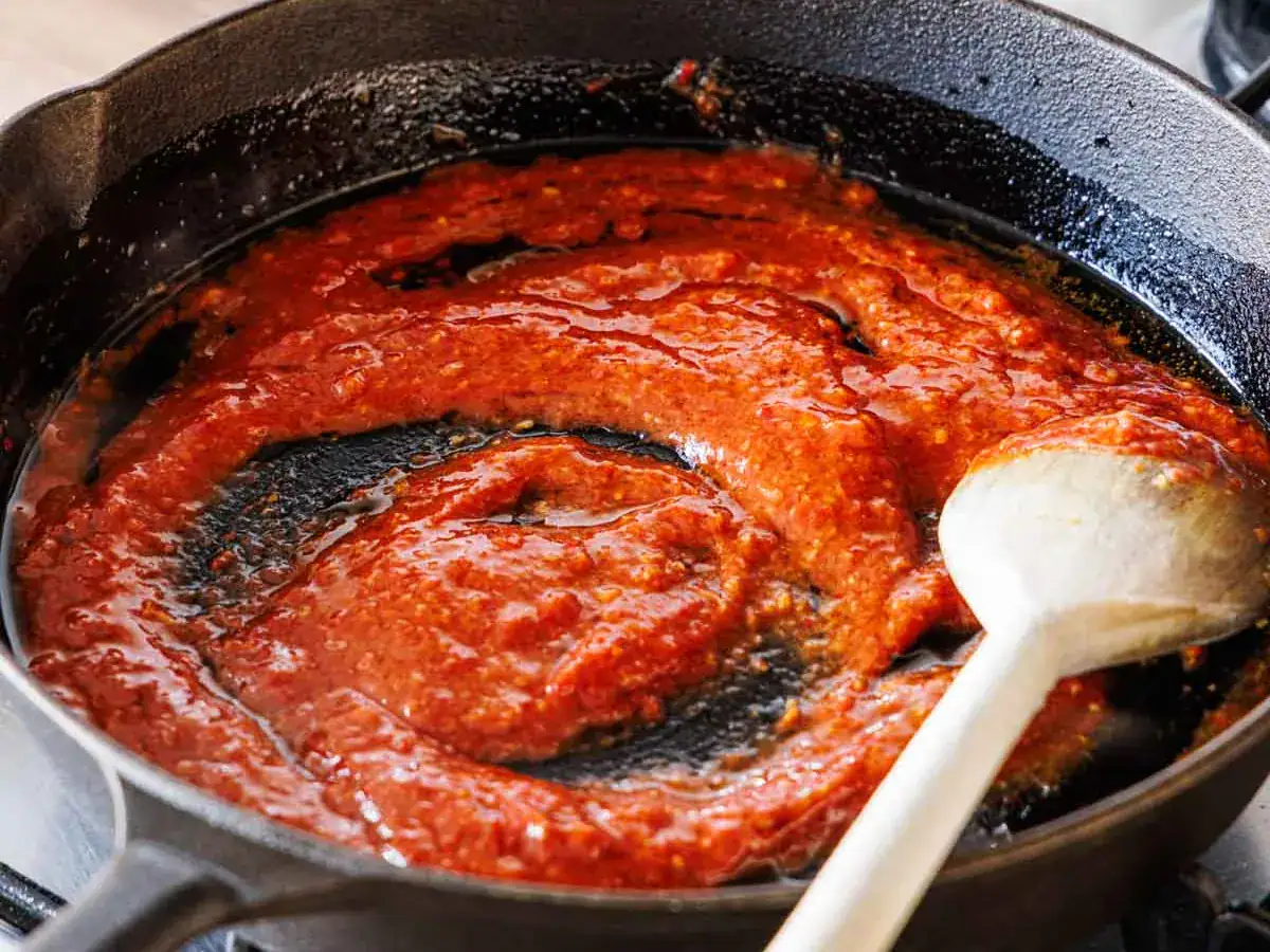 Tomato paste, chili paste, soy sauce, and other ingredients reducing in pan.