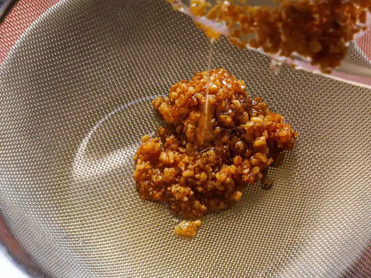 Fried garlic and oil being strained through mesh colander.
