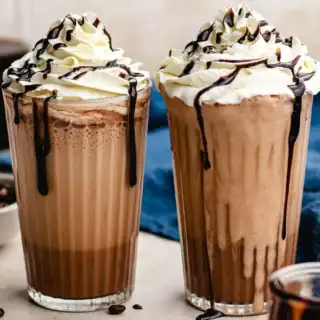 Two blended coffee drinks in glass with whipped cream topping.