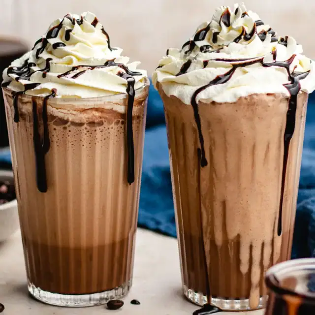 Two blended coffee drinks in glass with whipped cream topping.