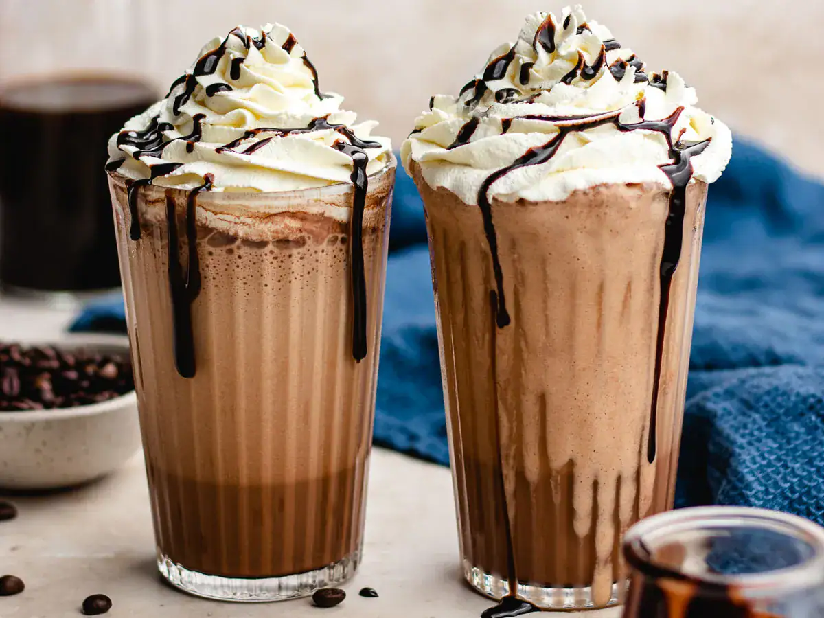 Two blended coffee drinks in glass with whipped cream topping.