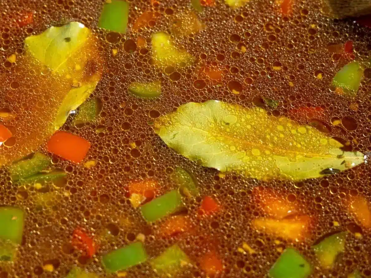 Broth with diced vegetables and bay leaf.