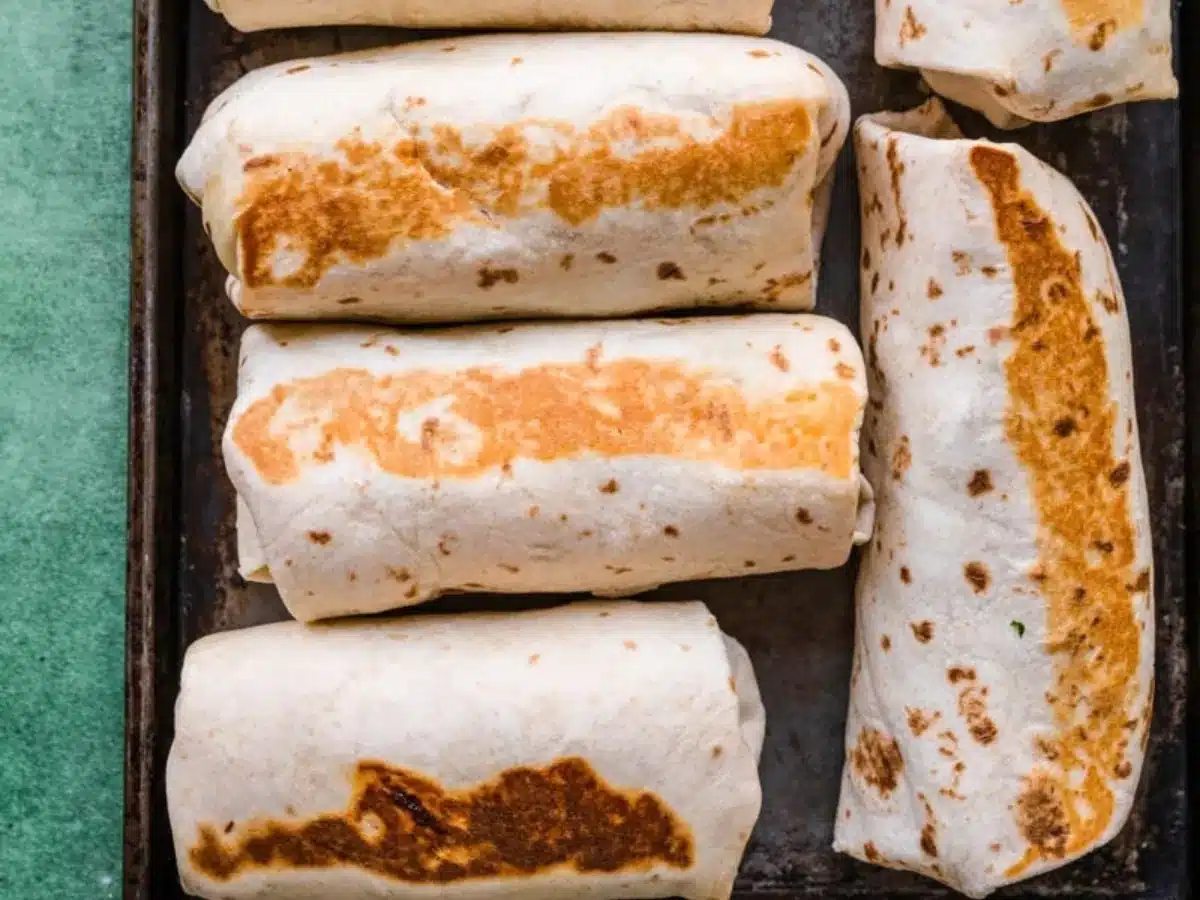 Browned burritos assembled on baking sheet.