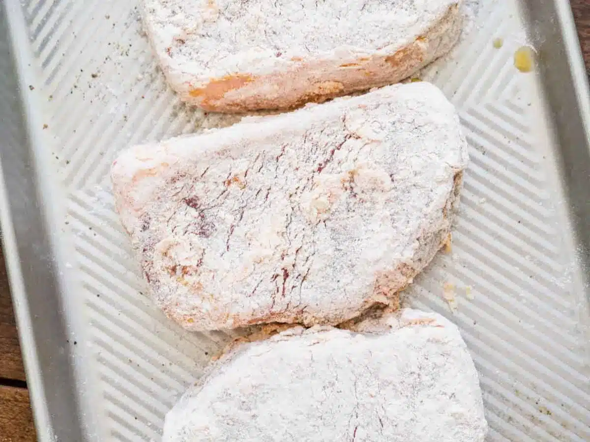 Seasoned flour coating raw meat fillets.