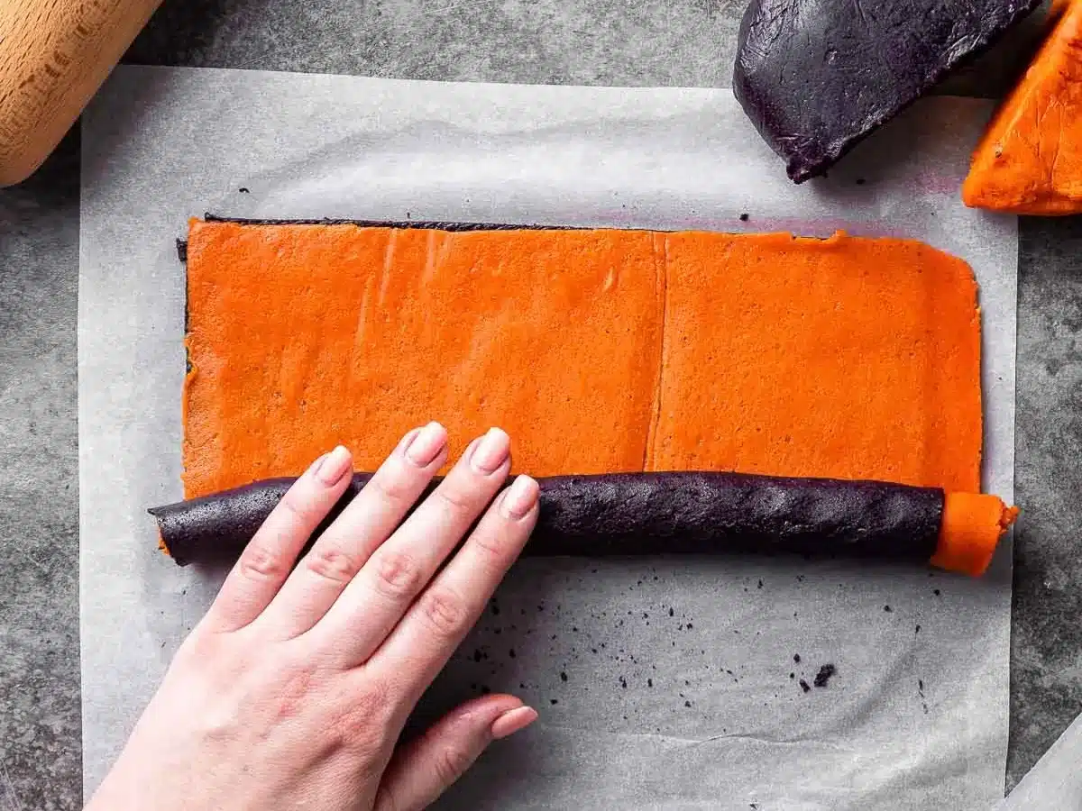 Purple and orange dough being rolled into log.