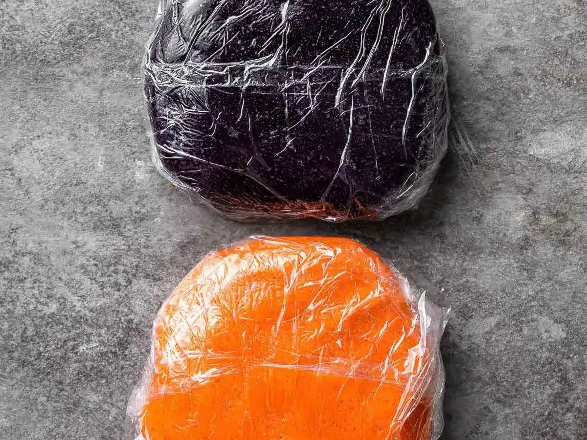 Purple and orange dough wrapped separately in plastic wrap.