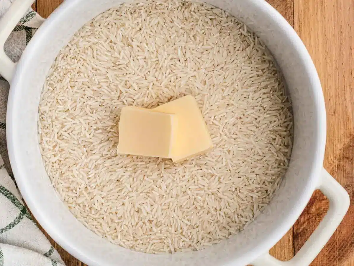 Uncooked rice in pot with two pats of butter.