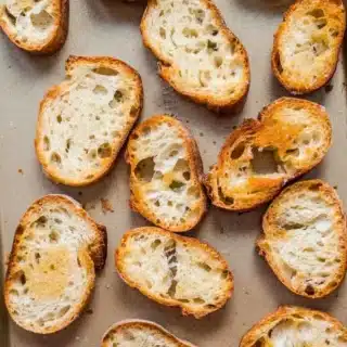 Slices of toasted baguette on baking sheet.