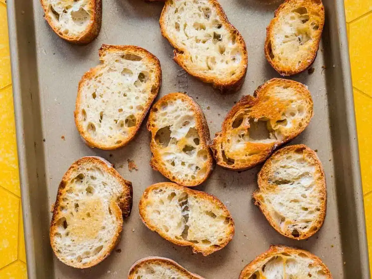 Slices of toasted baguette on baking sheet.
