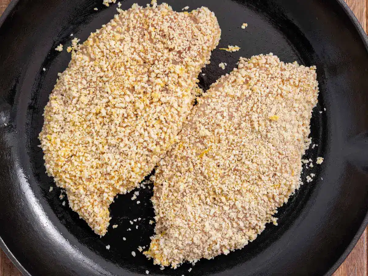 Chicken breast coated in bread crumbs, frying in pan.