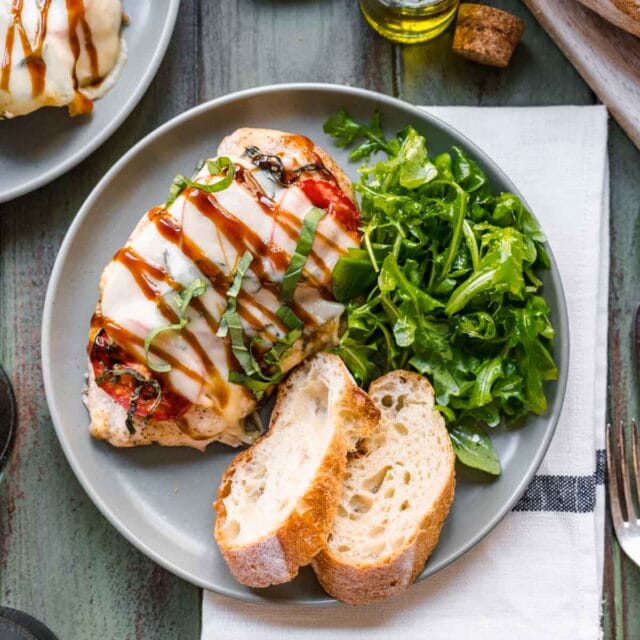 1 caprese chicken on a plate with a side salad and crusty bread