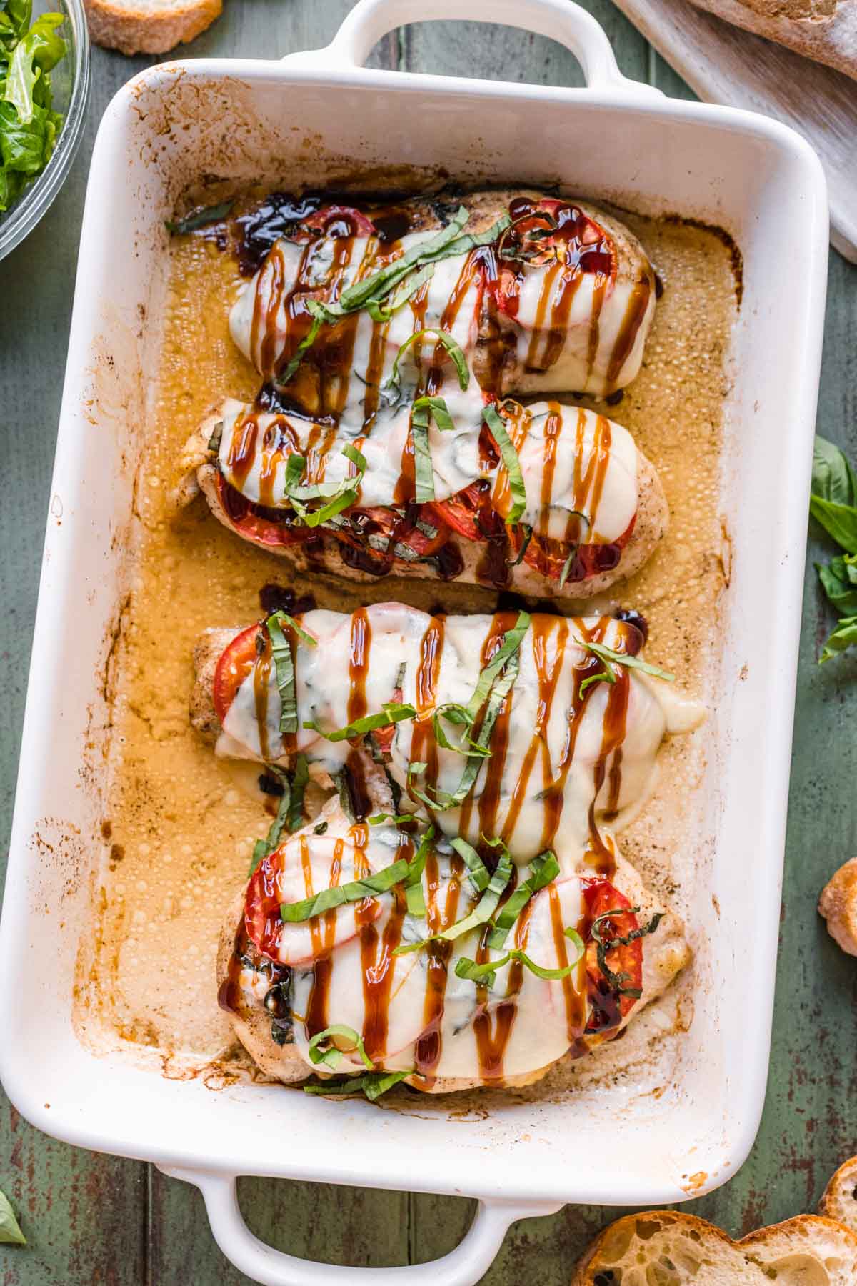 melted cheese on chicken topped with sliced tomatoes and basil in a cooking dish